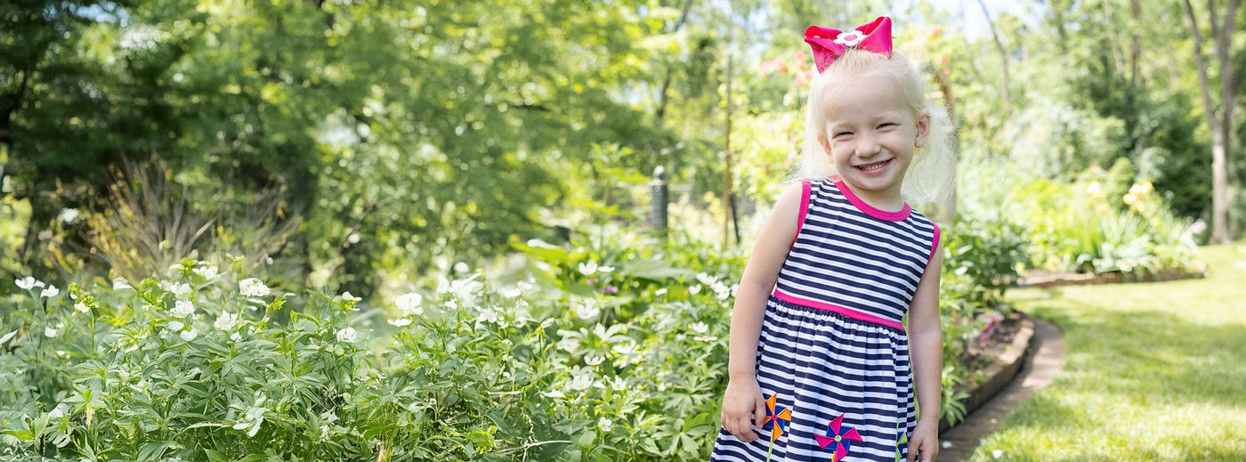 young girl in garden wearing striped dress with pinwheels