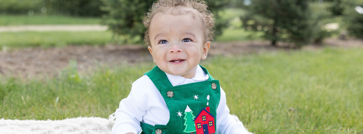 toddler sitting on a picnic blanket with a green holiday longall on