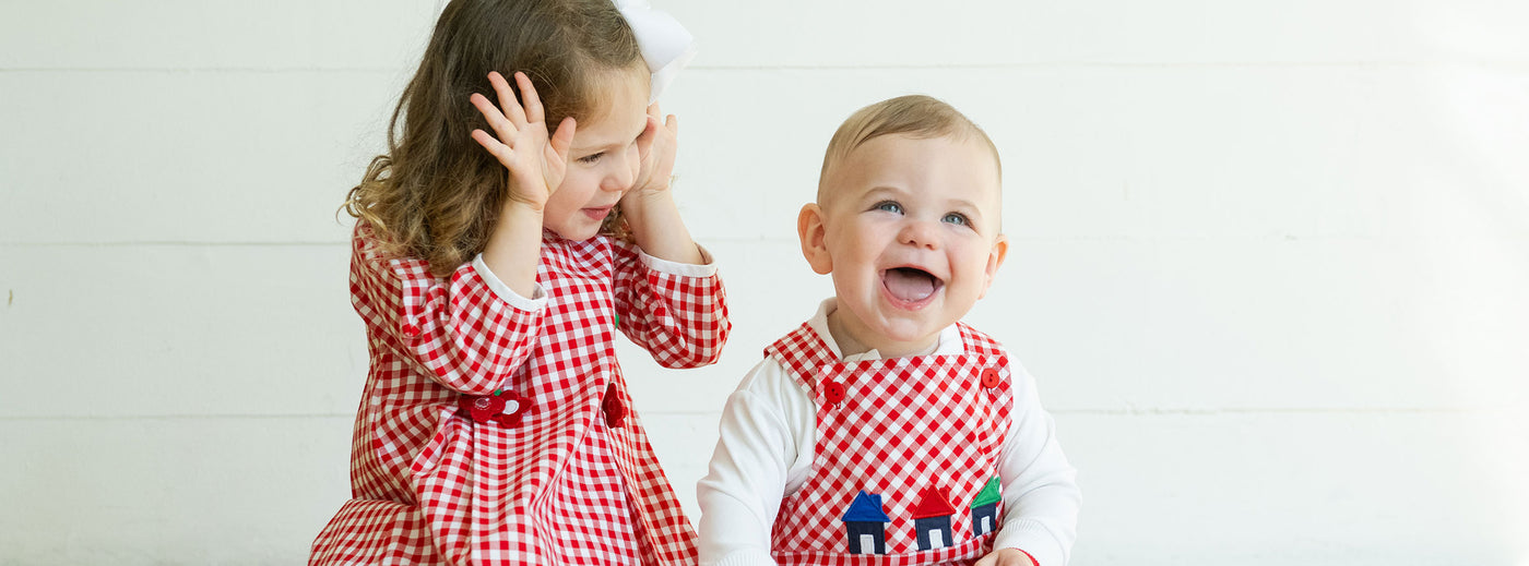 a young girl and a baby playing peekaboo in red gingham outfits