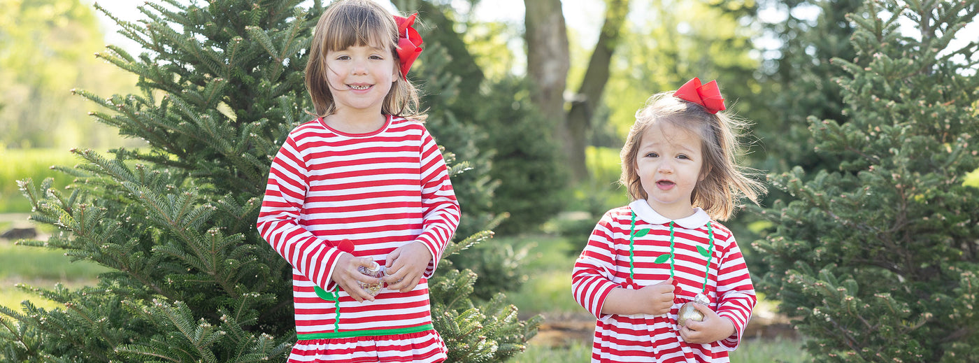 two girls in red stripe outfits and red bows at a tree farm