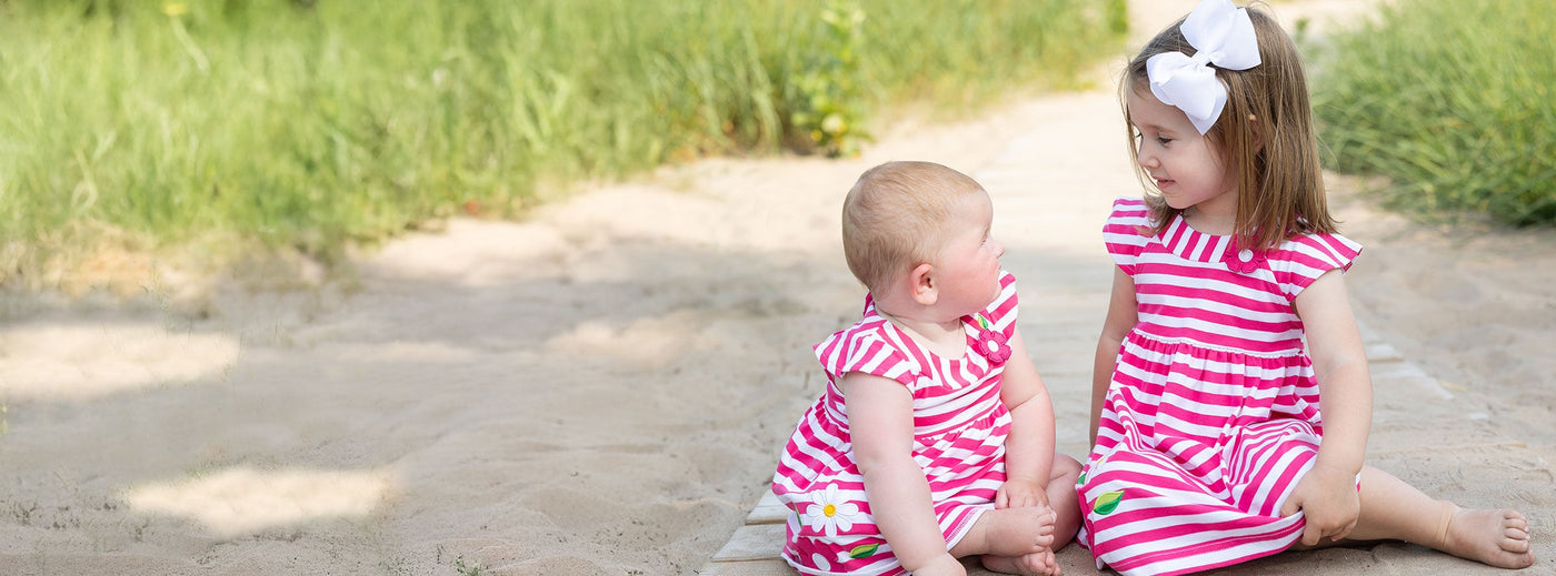 two young girls in pink and white stripe dresses on the beach