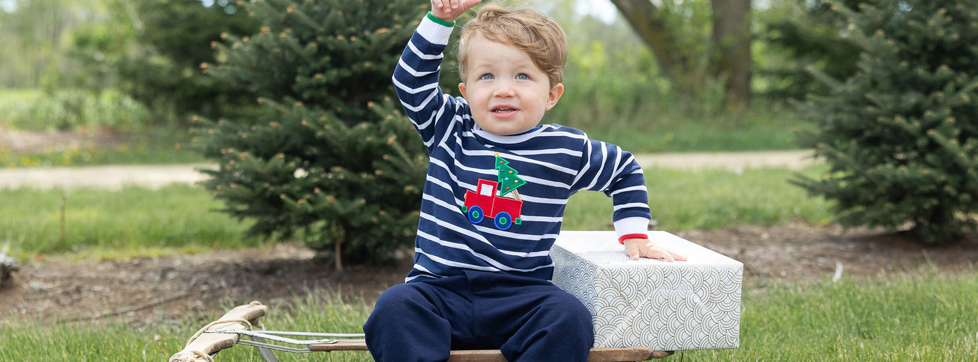 toddler boy sitting on a sled with a gift in a stripe shirt