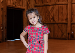 tween standing and smiling in a plaid dress