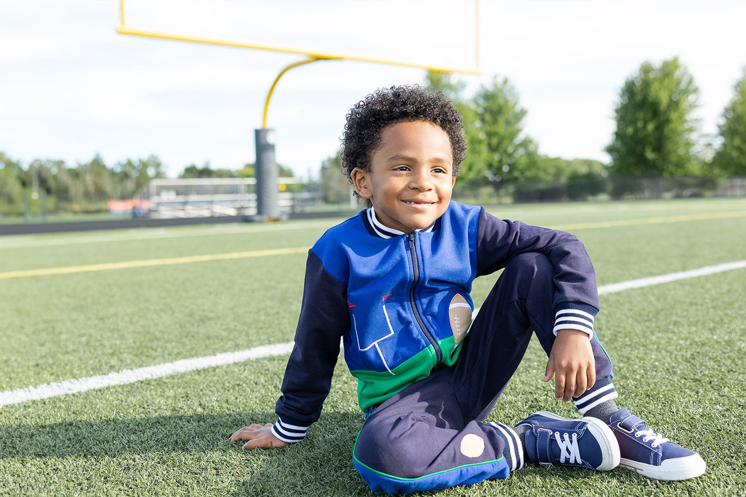 young boy in football themed jacket set sitting on football field