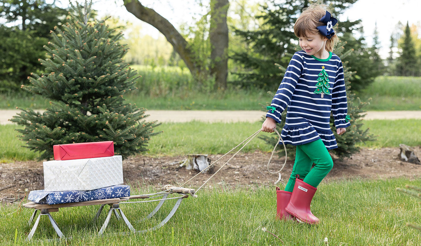 girl in holiday garments pulling a sled filled with gifts