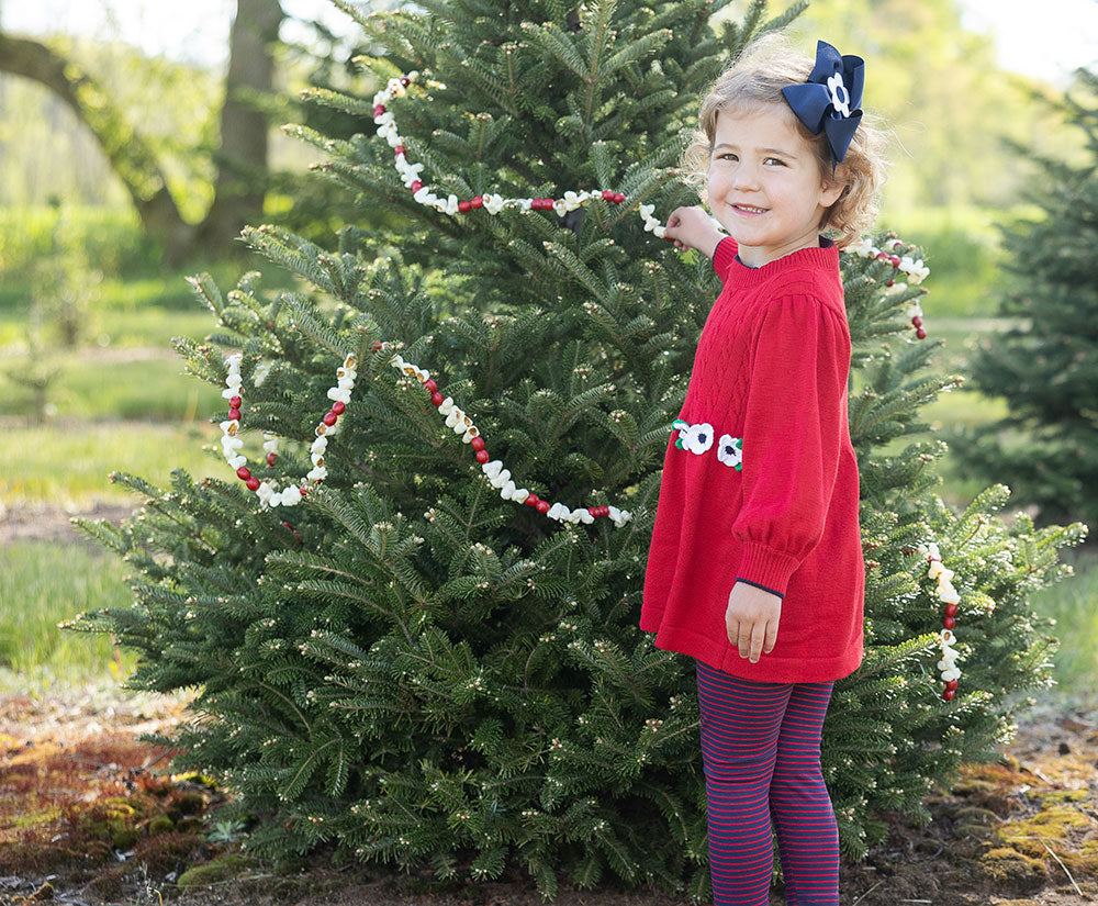 young girl with blue bow and red tunic in front of a decorated tree