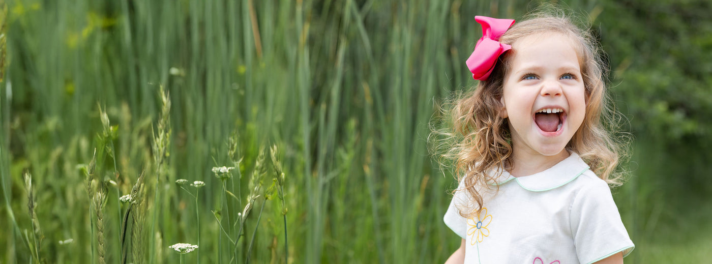 young girl in pink bow smiling outside